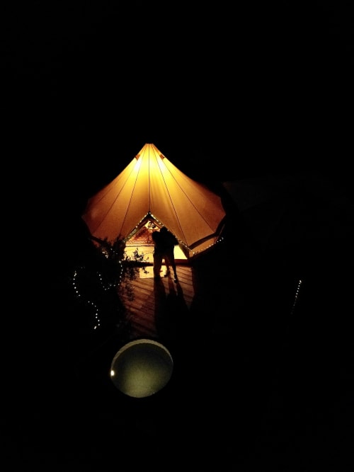 Tente illuminée à l'Agritusmo Stecadò de Dolceacqua avec silhouette d'une personne, lumière chaude contre le ciel nocturne