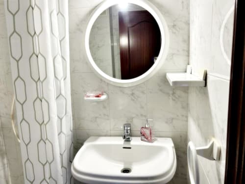 Moderno lavabo de baño con espejo redondo iluminado en el hotel Holibai de Baiona, España