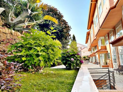 Jardín en terraza del apartamento Holibai en Baiona con plantas exuberantes, muros de piedra y entrada con vistas al mar en día soleado