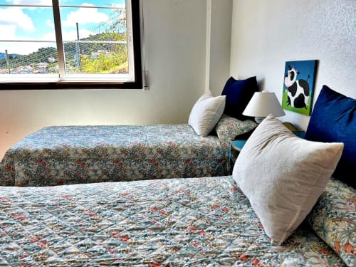 Habitación luminosa con camas gemelas, ropa de cama estampada y vistas al mar en apartamento de Baiona