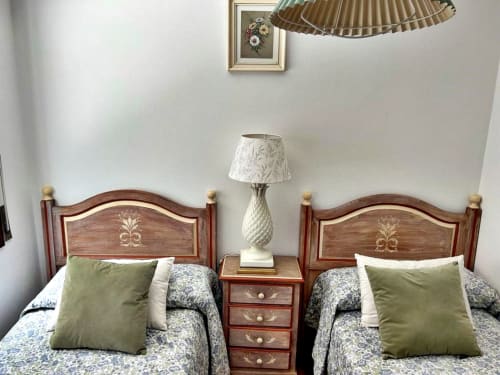 Dos camas individuales con cabeceras de madera en apartamento con vistas al mar en Holibai, Baiona, con almohadas verdes y lámpara de noche