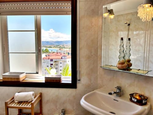 Baño con ventana con vista al mar en apartamento de Baiona, con lavabo, espejo, repisa y paisaje escénico