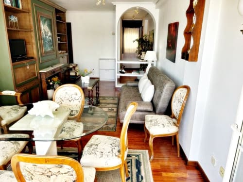 Elegante sala de estar con vistas al mar en Baiona, amueblada con sillas de madera, sofá, televisor y zona de comedor