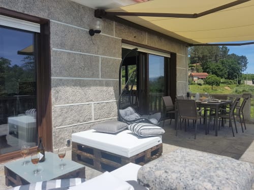 Terraza de la casa de alquiler vacacional O Eido de Celia, en Guláns, Ponteareas, Galicia, con muebles de exterior, zona de comedor al aire libre y sofás bajo un toldo, ideal para disfrutar de un entorno tranquilo y natural.