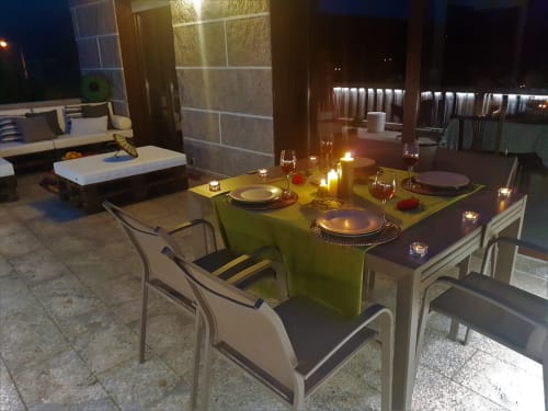 Terraza iluminada por la noche en la casa de alquiler vacacional O Eido de Celia, en Guláns, Ponteareas, Galicia, con mesa de comedor al aire libre decorada con velas, copas de vino y ambiente acogedor, ideal para cenas al aire libre.