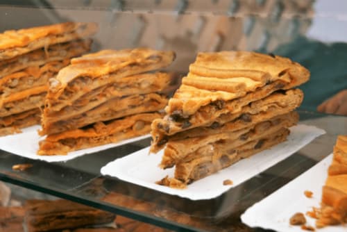 Imagen de porciones de empanada gallega apiladas en platos blancos, una especialidad gastronómica típica de Galicia, servida en la VUT 'O Eido de Celia' en Ponteareas, Pontevedra. Esta casa de alquiler vacacional ofrece una experiencia auténtica en un entorno natural gallego, ideal para disfrutar de la cocina tradicional y el turismo rural. Más información en www.oeidodecelia.com.