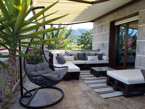 Terraza acogedora en la VUT 'O Eido de Celia' en Guláns, Ponteareas, Pontevedra, equipada con un amplio sofá en forma de L, cojines decorativos, mesa de centro y una silla colgante para relajarse. La terraza está decorada con una alfombra de rayas y una planta, y cuenta con una sombrilla retráctil que proporciona sombra. Desde la terraza se disfruta de vistas al entorno natural gallego, creando un espacio ideal para el descanso al aire libre. Más información en www.oeidodecelia.com.