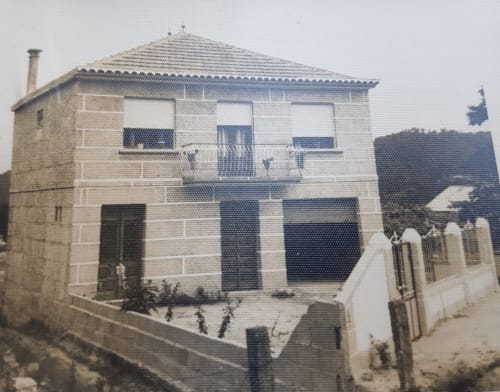 Fotografía en blanco y negro de 1969 que muestra la primera construcción de lo que hoy es la VUT O Eido de Celia en Galicia. La casa, de dos pisos y construida en piedra, cuenta con un pequeño jardín cercado en el frente y un balcón central en la planta superior. Esta imagen histórica captura los orígenes de una vivienda tradicional que con el tiempo se ha convertido en un alojamiento turístico.