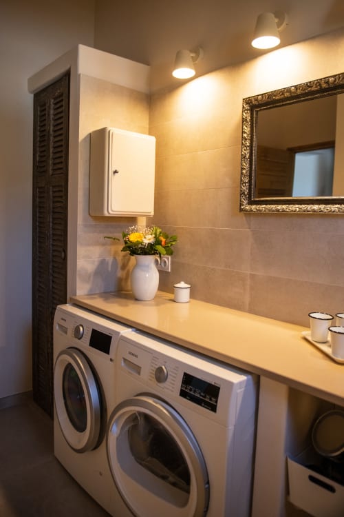 Well-equipped laundry area with washing machine, dryer, and stone countertop at Bastide Toujours Dimanche, Gordes, Luberon, Provence, France.