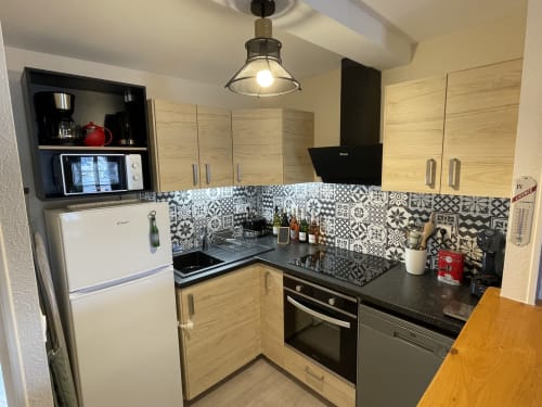 Moderne Küche mit hellem Holzschrank, schwarzen Arbeitsplatten, gemustertem Fliesenspritzschutz und Edelstahlgeräten bei Gites