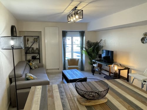 Gemütliches Wohnzimmer in den Gîtes des Trois Provinces mit grauem Sofa, Fernseher, Essbereich und Terrassenblick