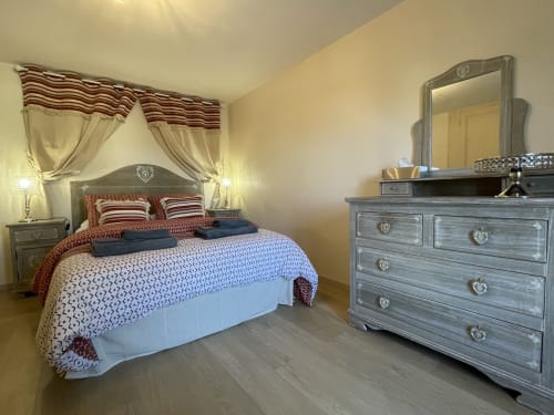Elegantes Schlafzimmer in den Gîtes des Trois Provinces mit gestreiften Vorhängen, gemusterter Bettwäsche, grauer Kommode mit Spiegel und warmer Atmosphäre