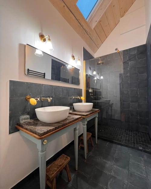 Modern bathroom at Domaine du Tertre Ychot with dual vessel sinks, black tile, brass fixtures, and skylight