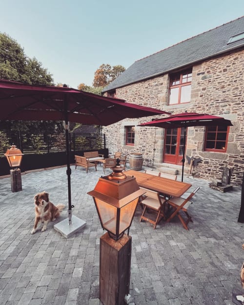 Outdoor courtyard at Domaine du Tertre Ychot in Dol de Bretagne with stone buildings, red awnings, seating, and a dog