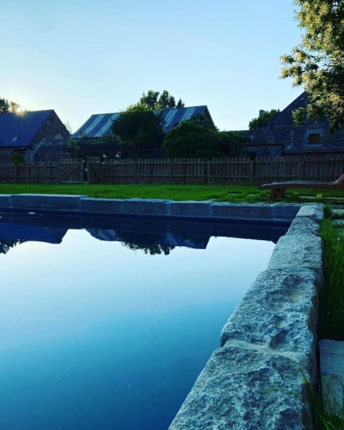 Stone bridge over calm water with historic stone buildings and green grounds at Domaine du Tertre Ychot, Dol de Bretagne