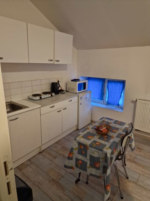 Petit studio cuisine à la Résidence Mantekila à Marcinelle avec table à manger, armoires blanches et vue sur la ville.