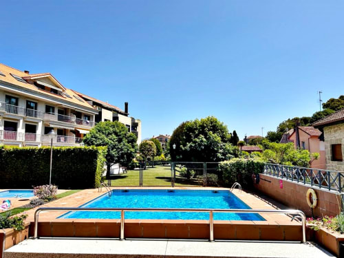 Piscina radiante en la urbanización familiar Baiona con tumbonas, setos circundantes y edificios de apartamentos