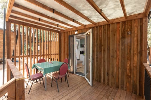 Terrasse couverte en bois avec table de repas et chaises au Camping La Lézardière, vue sur jardin