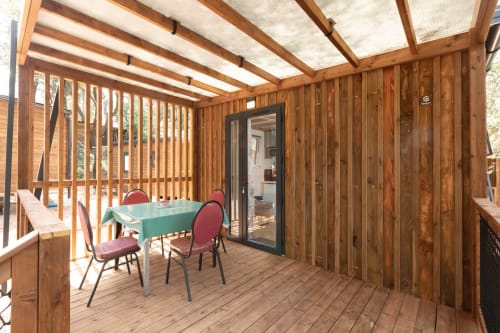 Solarium en bois au Camping La Lézardière avec table turquoise, chaises rouges et baie vitrée donnant sur le jardin à La Valette du