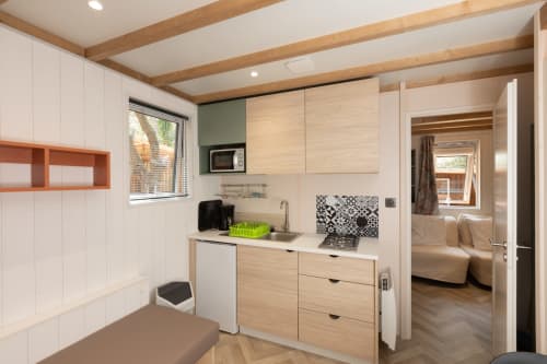 Petite cuisine moderne du Camping La Lézardière avec meubles en bois, évier, cuisinière et accès au séjour