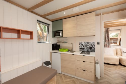 Kitchenette moderne aux armoires bois, murs blancs et poutres apparentes dans un appartement camping à La Lézardière, La Valette