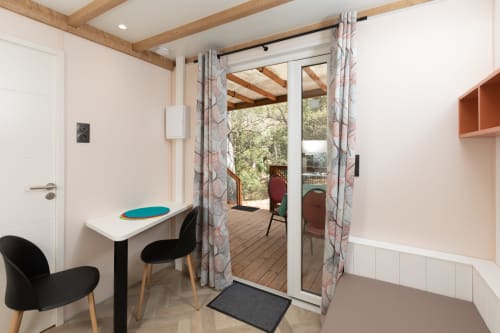 Intérieur moderne de l'appartement au Camping La Lézardière avec bureau, chaises noires et baie vitrée ouvrant sur balcon vue jardin