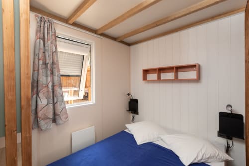 Chambre confortable au Camping La Lézardière avec literie bleue, poutres en bois et vue sur La Valette du Var