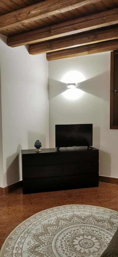 Modern Palermo apartment living room with exposed wooden beams, flat-screen TV on black console, white walls, and decorative