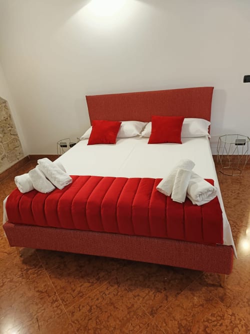 Modern bedroom at Casa Bellini Palermo with red upholstered bed, white linens, red pillows, and wooden flooring