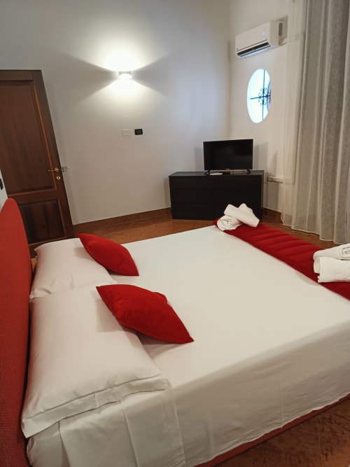Modern bedroom at Casa Bellini in Palermo with white bed, red pillows, flat-screen TV, air conditioning, and city view window