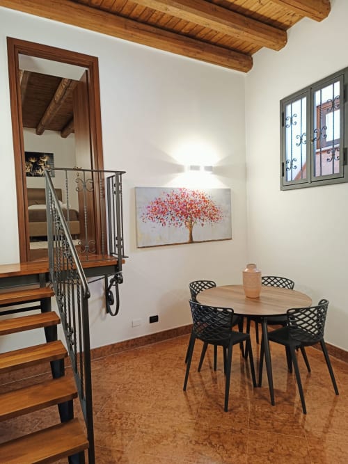 Dining room with round wooden table, modern black chairs, and red tree artwork at Casa Bellini apartment in Palermo