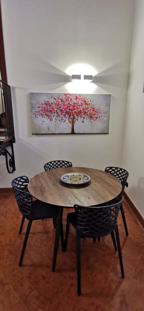 Modern dining room at Casa Bellini Palermo with round wooden table, black chairs, and red flower tree artwork under ceiling
