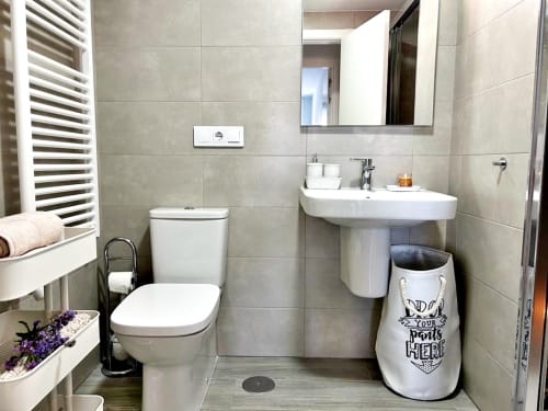 Baño moderno en apartamento de Baiona con inodoro, lavabo de pedestal, espejo, toallero calefactor y área de ducha