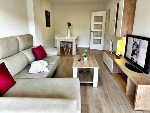 Sala de estar moderna en Baiona con sofá beige, televisor, comedor y piso de madera