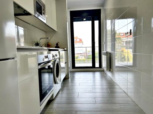 Cocina moderna del apartamento Bon Xeito en Baiona con armarios blancos, lavadora, horno y vistas al balcón