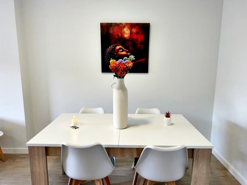 Moderna zona de comedor en apartamento Holibai con mesa blanca, sillas, obras de arte y flores sobre pared blanca en Baiona.