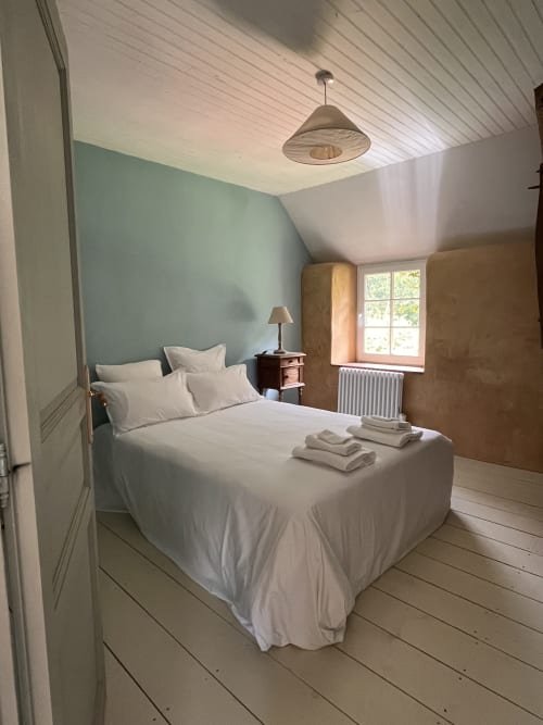 Bright bedroom at Domaine du Tertre Ychot with white bed, mint green accent wall, wooden floors, and natural light from