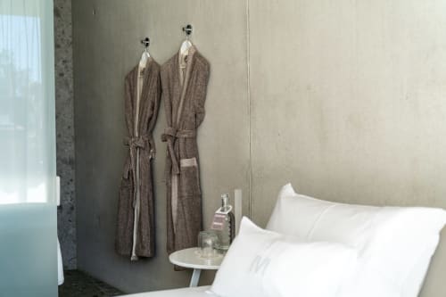 Modernes Hotelzimmer im Le Pavillon M mit weißen Kissen, grauen Bademänteln an Wandhaken und Nachttisch mit Toilettenartikeln
