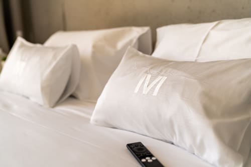 Luxuriöse weiße Kissen mit Monogramm auf einem Bett im Boutique-Hotel Le Pavillon M in Grignan, Frankreich