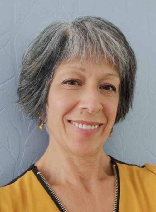 Femme souriante aux cheveux gris portant une veste jaune et noire à la maison d'hôtes Au Gîte d'Isigny