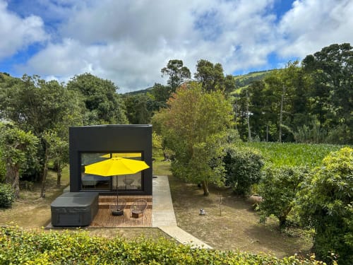 Modern black cabin with yellow umbrella and hot tub at Villa Várzea, surrounded by lush greenery in Várzea, Portugal