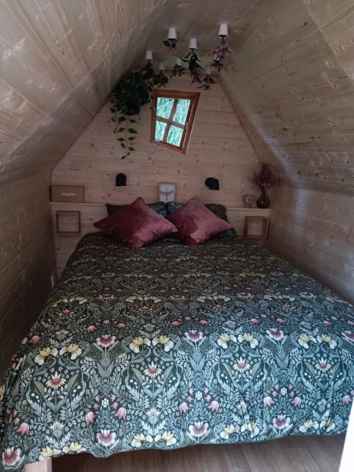 Chambre douillette au chalet en bois aux Refuges Du Chalet à Jalhay, avec literie fleurie et plantes suspendues