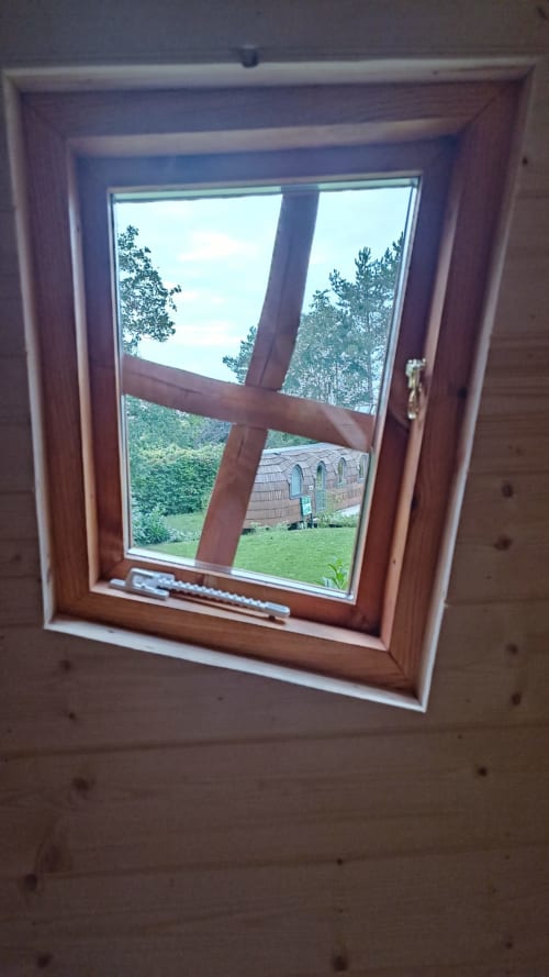 Fenêtre en bois du gîte Les Refuges Du Chalet donnant sur le jardin avec arbres et structure en bois