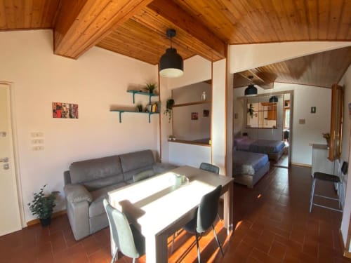 Zona giorno moderna presso L'Appartamento Giusto, Bologna, con soffitto in legno, divano grigio e tavolo da pranzo