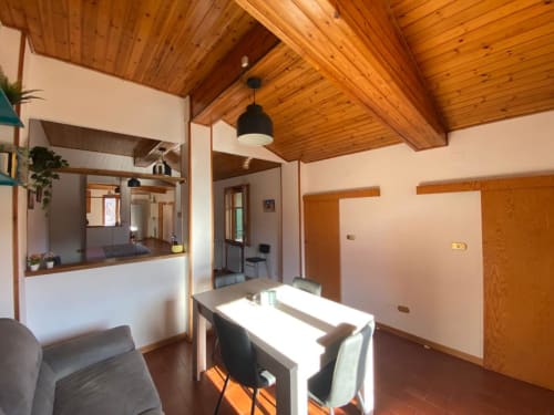 Zona living moderna con travi a soffitto in legno, tavolo da pranzo e cucina aperta nell'appartamento Social Costa presso L'Appartamento