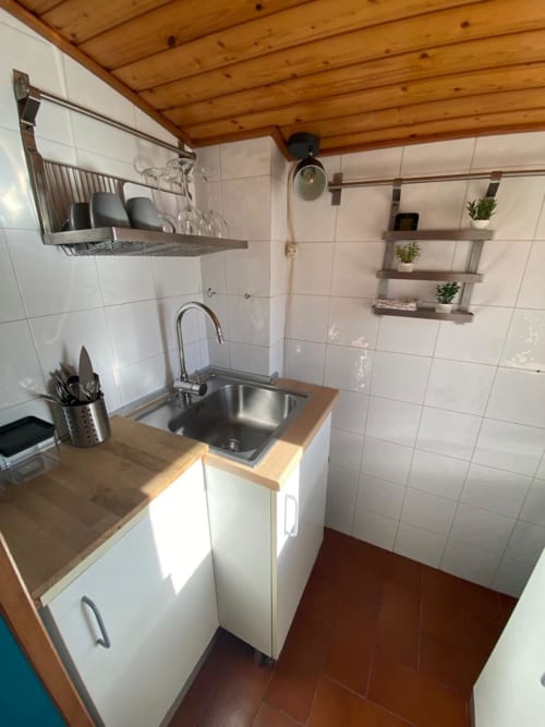 Cucina compatta in BnB a Bologna con piastrelle bianche, soffitto in legno, lavello in acciaio inossidabile, scaffali e banco pranzo