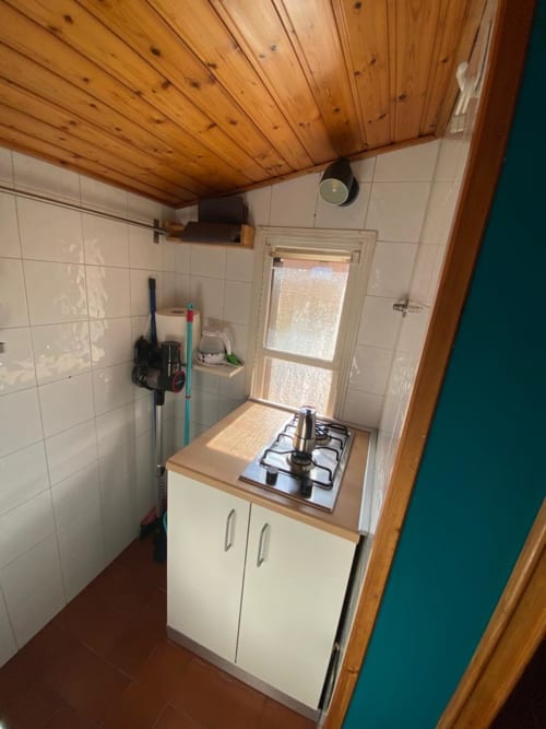 Cucina compatta in appartamento bolognese con piano cottura a gas, soffitto in legno, mobili bianchi e pareti piastrellate
