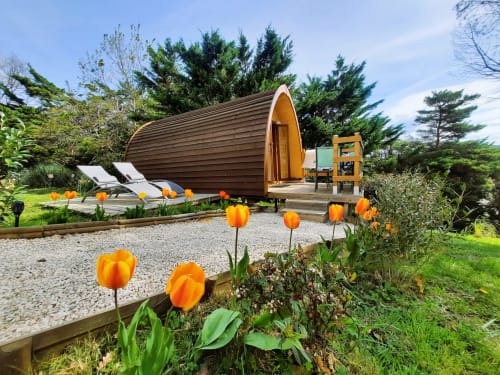Barrel-shaped glamping pod at Belloréade with orange tulips, lounge chairs, and forested backdrop