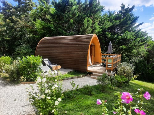 Wooden barrel glamping pod surrounded by lush gardens with flowers at Belloréade in Belloc, France