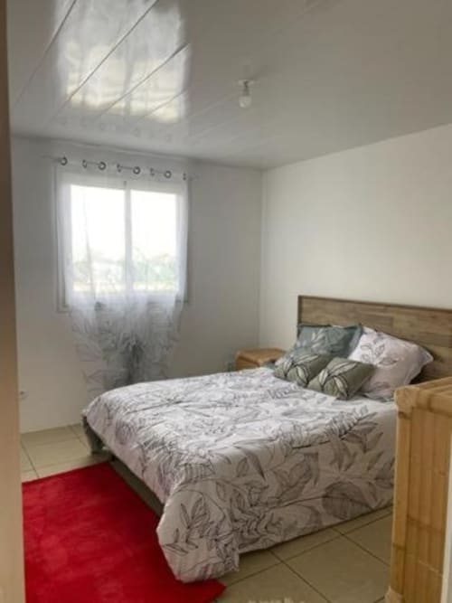Chambre lumineuse du Case Vi D'O' B&B à La Plaine des Cafres avec lit en bois, tapis rouge et lumière naturelle
